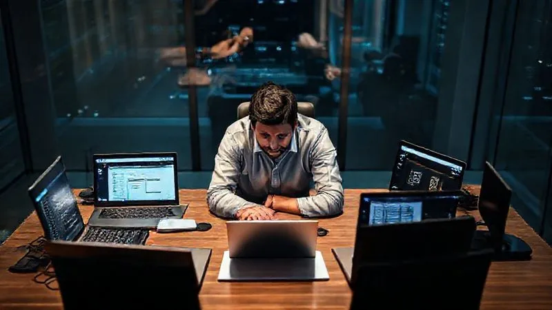 Photorealistic, professional photography, 8K, cinematic lighting, sharp focus, depth of field, shot on a high-end DSLR. A person sitting at a modern desk, surrounded by multiple open laptops and a tablet, each displaying different types of work (e.g., coding, writing, graphic design), symbolizing diverse income streams. The person looks focused and industrious.