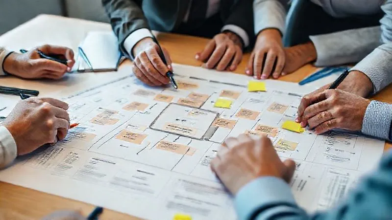 A photorealistic image of hands collaborating around a detailed project plan or flowchart on a table, with highlighted sections for "Corrective Actions" and "Timelines," surrounded by pens and sticky notes, professional office setting, cinematic lighting, sharp focus, depth of field, 8K hyper-detailed.
