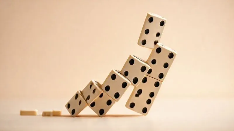 A photorealistic, professional photography, 8K image depicting a single large domino falling, triggering a chain reaction of smaller dominoes tumbling in its wake, against a clean, minimalist background. Cinematic lighting emphasizes the cascading effect, sharp focus on the falling dominoes, depth of field blurring the distant ones to highlight the immediate impact. Shot on a high-end DSLR.