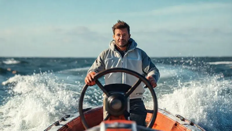 A photorealistic, professional photography, 8K image of a person standing calmly and confidently at the helm of a small boat, navigating through choppy but manageable waters under a clearing sky. Cinematic lighting emphasizes their steady gaze and the subtle strength in their posture, sharp focus on the person and the immediate boat, depth of field blurring the tumultuous background to symbolize control amidst challenges. Shot on a high-end DSLR.